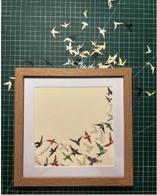 A framed piece of laser-cut paper birds in flight on a green cutting mat